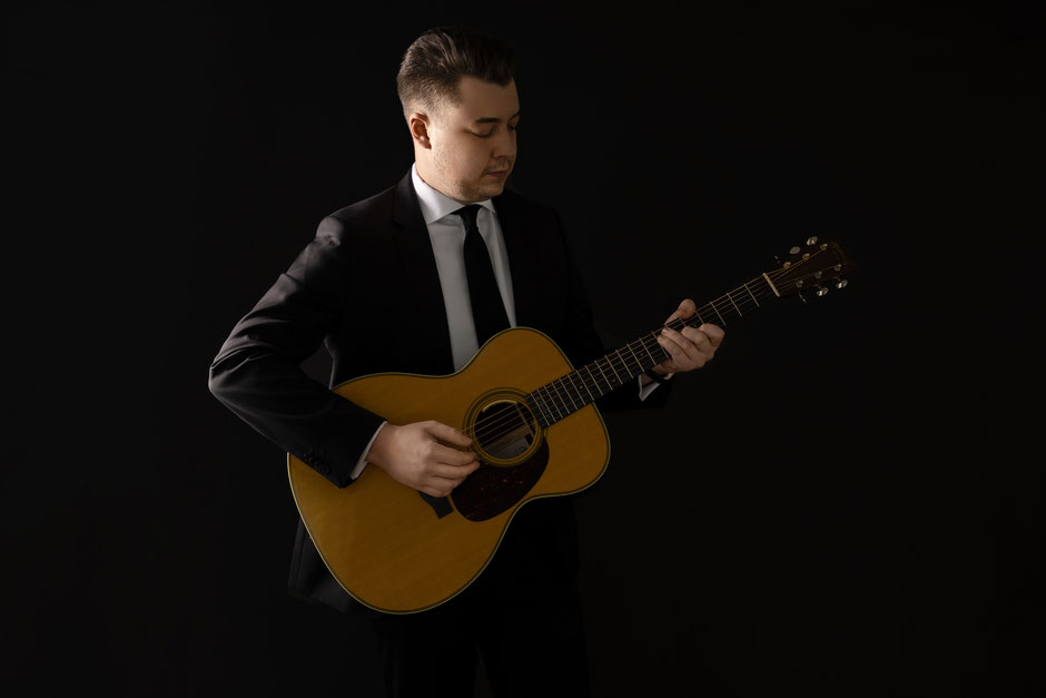 A picture of our artist Julian Wolf playing the guitar with a black background.