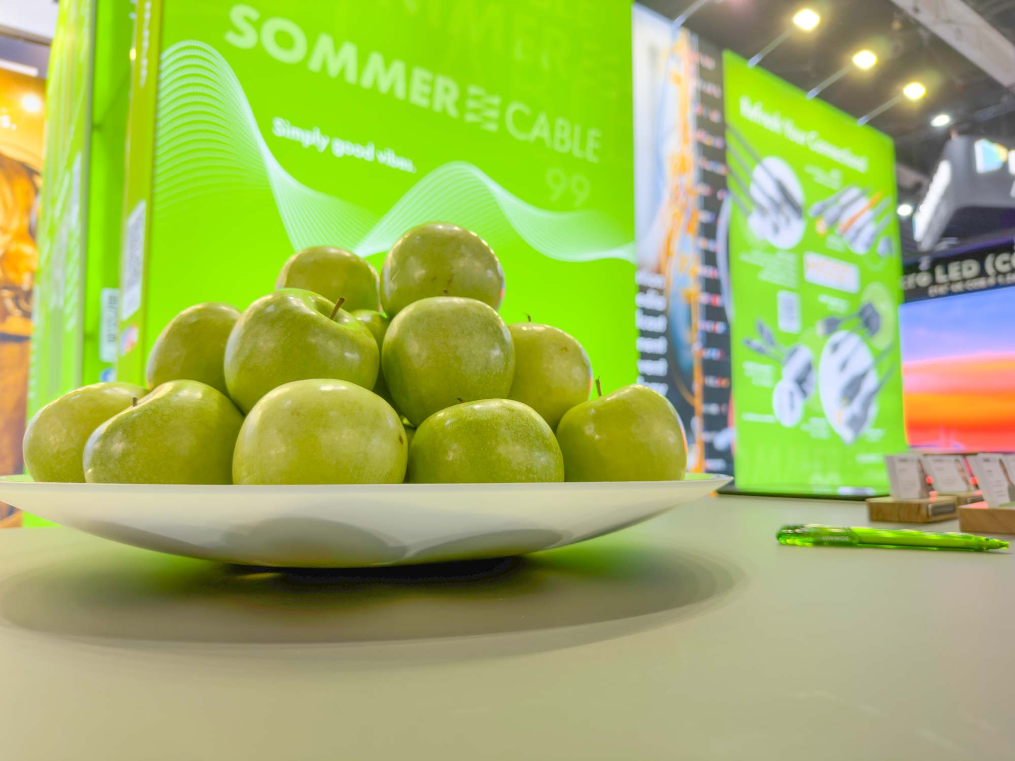 A plate of green apples on a table. In the background you can see our summer cable fair stand.