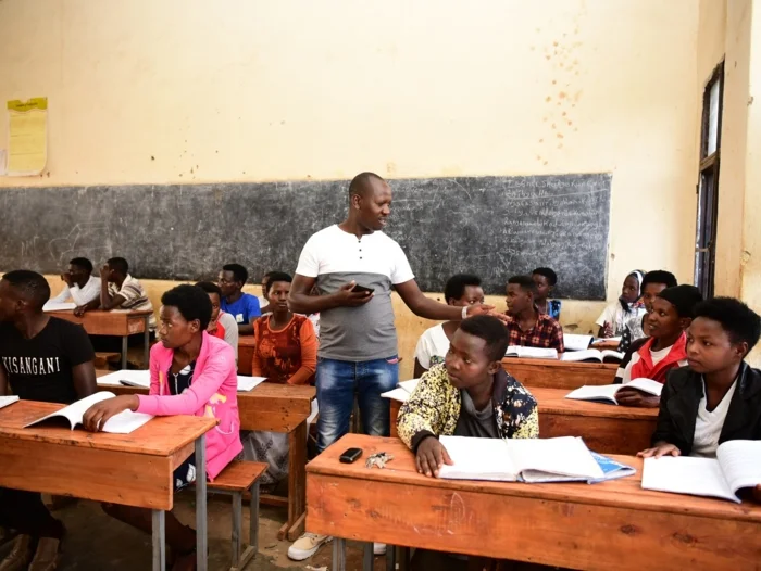 Ein Bild von unserem Schul-und Bildungsprojekt eQUiP-Magu in Ruanda. Abgebildet ist eine Schulklasse. Der Lehrer steht in der Mitte und die Schüler sitzen an ihren Tischen. 