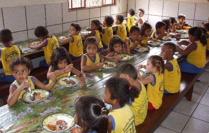 Mehrere Kinder sitzen in gelben T-Shirts an einem langen Tisch und essen.