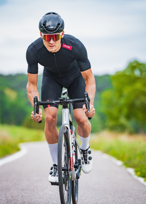 Profi-Triathlet Samuel Boettinger beim Fahrrad fahren auf einem Weg. Im Hintergrund sind Wälder zu sehen.