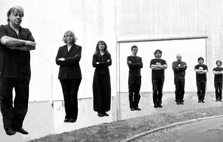 A black and white group photo of our eight artists from the band “Magma” standing next to each other with their arms crossed and looking into the camera.