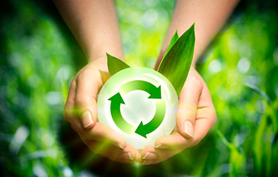 An image of the recycling symbol, held by two hands. A slightly blurred meadow can be seen in the background.